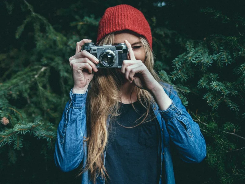 Девушка в красной шапке и джинсовой рубашке фотографирует