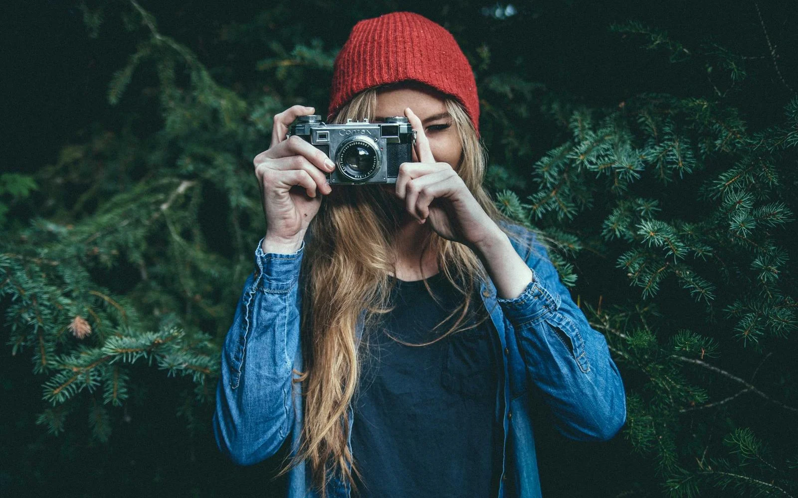 Девушка в красной шапке и джинсовой рубашке фотографирует